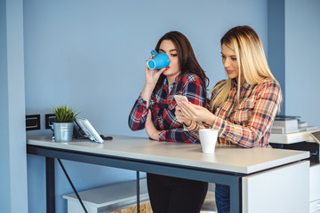Girl peeking at colleagues mobile phone while drinking coffee