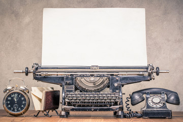 Retro aged black typewriter with large paper blank, classic telephone, old alarm clock and mail...