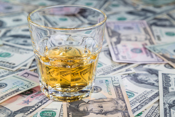 glass of whiskey is on dollar bills of different denominations