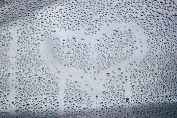 Heart and raindrops. Drawn romantic blurred love symbol drawn by hand on the wet window glass, light background