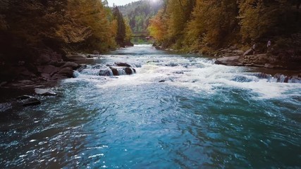 Low flight over the mountain river, blue in the middle of the forest and mountains. Sunset time. The sun's rays give orange flare. The concept of curing urological diseases and prostatitis.