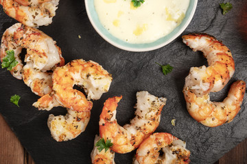 A closeup photo of cooked shrimps on a black plate with a sauce bowl