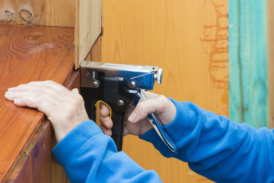 Persona que ensambla un mueble de madera, con ayuda de una grapadora