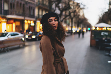 Obraz premium Successful business woman enjoying vacation in a small european city in the autumn time. Beautiful student girl wearing stylish clothes crossing road while going home at the evening.