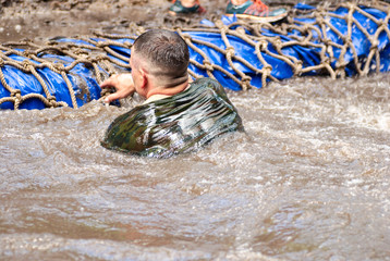 Man swiming in the moat during  a mud race with obstacle course.