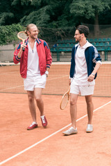 cheerful sportive friends with wooden rackets walking on tennis court