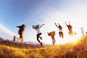 Group happy friends runs and jumps mountains sunset