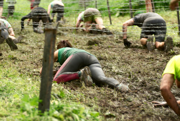 Female crawling under barbed wire during  a mud race with obstacle course.