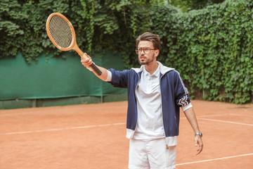 handsome tennis player pointing with wooden racket on tennis court