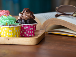 Colorful of homemade cupcake on wooden tray on and open book on wooden table. Concept of lifestyle and relax.