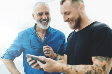 Professional IT specialist sharing with his idea with a manager showing his ideas on a mobile phone. Cheerful businessmen watching latest market indices of the company stock online on a smartphone.