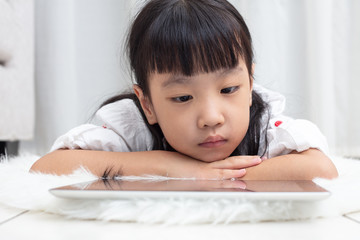 Fototapeta premium Asian Chinese little girl lying on the floor and playing tablet