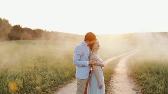 Bride and groom embrace and smile standing on a countryside road in a sunset light