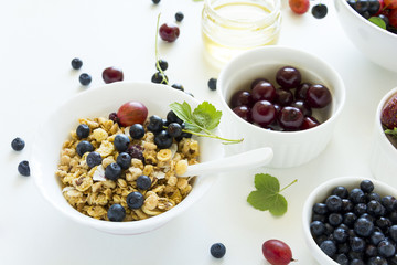 Bowl of homemade granola with strawberry, blueberry, cherry, gooseberry, black currant and honey on white wooden background. Top view. Flat lay. Copy space