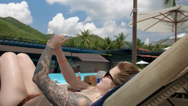 Young tattooed woman using her smartphone and taking pictures of herself lying on a lounger