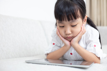 Asian Chinese little girl lying on the sofa and playing tablet