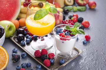 Many different fruits and berries. Vitamins and healthy food. Summer products and orange juice in a glass. Yoghurt and muesli with berries. Tasty breakfast. Copy space.