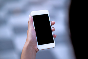 Mockup image of a woman holding and displaying a white mobile phone with a black screen with a blank screen on a table in a modern cafe. Ideas for working with communication tools.