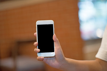 Mockup image of a woman holding and displaying a white mobile phone with a black screen with a blank screen on a table in a modern cafe. Ideas for working with communication tools.