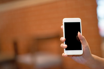 Mockup image of a woman holding and displaying a white mobile phone with a black screen with a blank screen on a table in a modern cafe. Ideas for working with communication tools.
