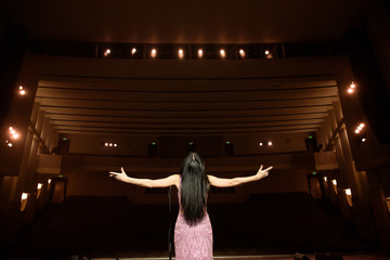Fototapeta na wymiar Beautiful caucasian woman singing with the microphone. back view girl in long gown performing on stage