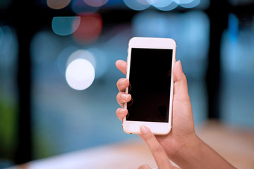 Mockup image of a woman holding and displaying a white mobile phone with a black screen with a blank screen on a table in a modern cafe. Ideas for working with communication tools.
