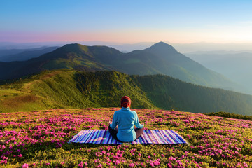 On the lawn among the rhododendron flowers the yoga girl is sitting in the pose on the colorful...