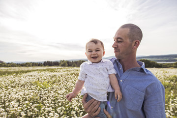 little boy and his father enjoying outdoors in field of daisy flowers