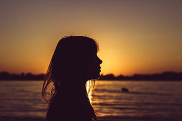 Silhouette of young woman sitting near the water on sand beach with sand in hands