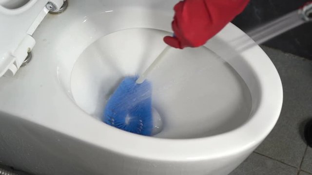 hand in gloves cleaning toilet bowl with brush