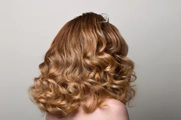 Photo sur Plexiglas Salon de coiffure Female hairstyle long curls on the head of the brown-haired woman looking back at the gray background turning the head to the right.