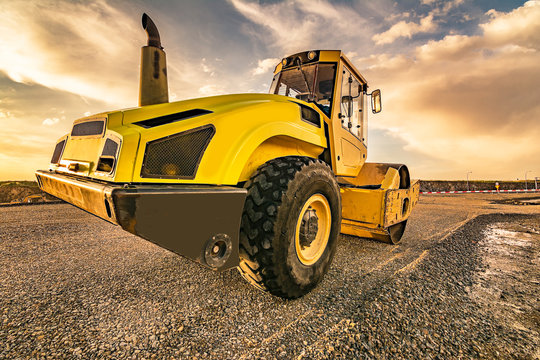 Yellow steamroller on asphalt road in sunlight