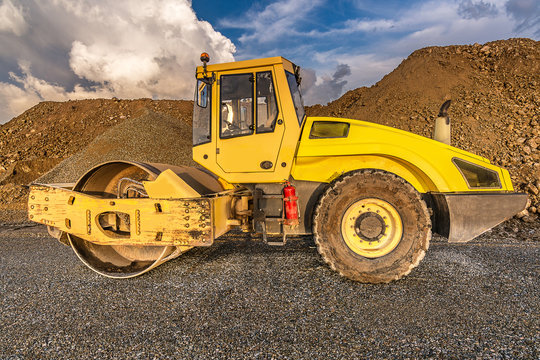 Yellow steamroller on asphalt road in sunlight