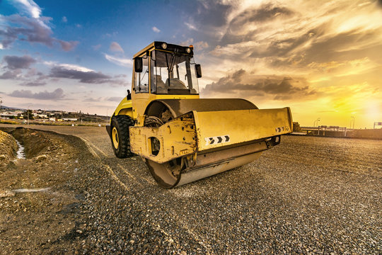 Yellow steamroller on asphalt road in sunlight