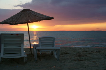 Thatched parasol and empty sunbeds in a beach at sunset time