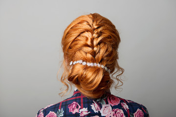 A female hairstyle is a low bun on a red-haired girl back view on a gray isolate.