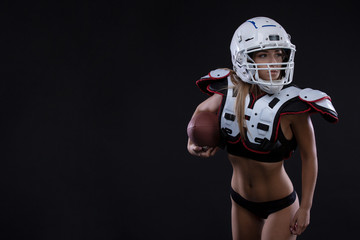 Sportive serious woman in helmet of rugby player holding ball in stuio on dark background. . Copy space