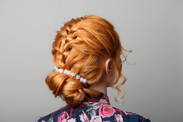 A woman's hairstyle is a low bun on a red-haired girl back view on a gray isolate turning the head...