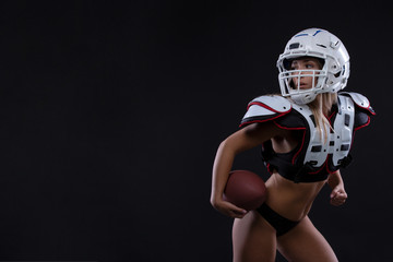 Sportive serious woman in helmet of rugby player holding ball in stuio on dark background. . Copy space