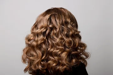 Cercles muraux Salon de coiffure Coiffure féminine de longues boucles sur la tête de la femme aux cheveux bruns vue arrière sur fond gris en tournant la tête vers la droite.