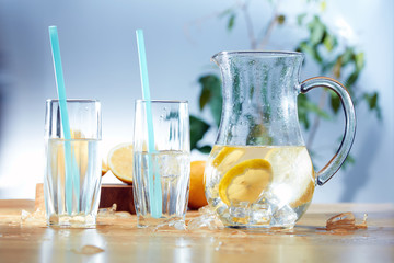 Decanter with sliced lemon, ice and glasses on wooden background