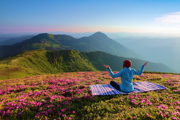 On the lawn among the rhododendron flowers the yoga girl is sitting in the pose on the colorful...