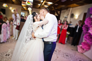 Happy wedding couple performing their first dance and kissing in restaurant in front of guests.