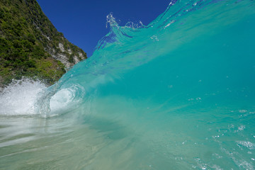 A crystal clear shorebreak wave on Klingking on Nusa Penida breaks on a tropical beach