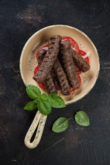 Serving pan with grilled cevapi or cevapcici sausages, top view on a dark brown stone background, vertical shot