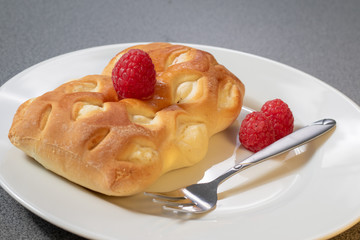 Ein braun gebackenes Teilchen dekoriert mit frischen Himbeeren auf einem weißen Kuchenteller