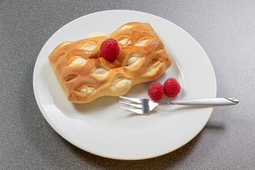 Ein braun gebackenes Teilchen dekoriert mit frischen Himbeeren auf einem weißen Kuchenteller