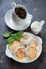 Curd fritters with coffee for breakfast, vertical shot on a brown stone background, selective focus