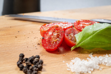 Nahaufnahme von halbierten Tomaten neben einem Basilikumblatt auf einem Holzbrett in der Küche