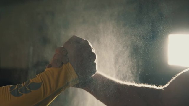 Two athletes shaking hands in gym while their hands are covered in magnesia. Hands of gymnast clapping white chalk powder in slow motion. Cloud against dark background